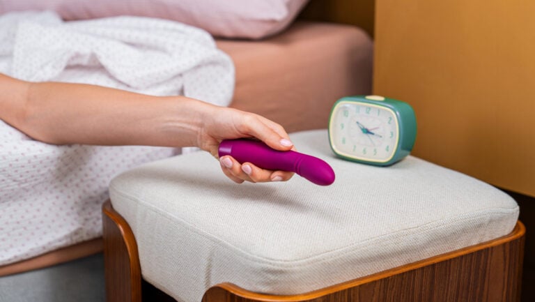 Une personne tient son premier vibromasseur dans sa main, au lit.