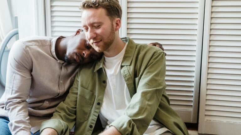 Un couple vit un moment intime à deux. La tête d'un des deux hommes repose sur l'épaule de son compagnon pendant qu'ils abordent une baisse de libido dans leur couple.