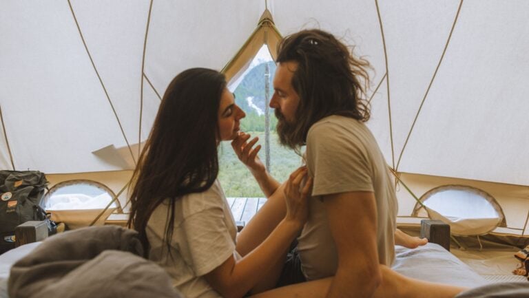 Deux personnes s'embrassent sous une grande tente bohème, cherchant à profiter du sexe au camping.