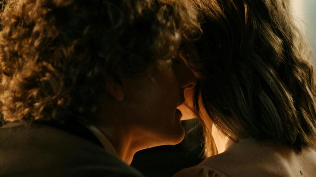 A la lumière d'une chandelle, un homme aux cheveux frisés chuchote et pratique le Dirt Talk à l'oreille d'une femme avec un carré mi-long.