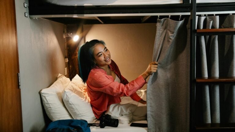 Une jeune femme est allongée dans le lit de son auberge de jeunesse, souriant et regardant avec qui elle pourrait vivre une histoire érotique.
