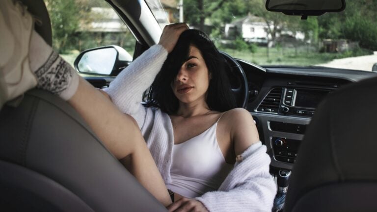 Une jeune femme se passe la main sensuellement dans les cheveux, assise dans voiture, prête à vivre une chaude histoire érotique.