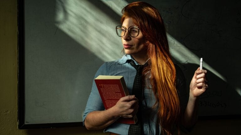 Une professeur séduisante se tient debout devant le tableau noir, un livre et un style à la main, prête à vivre une histoire érotique.