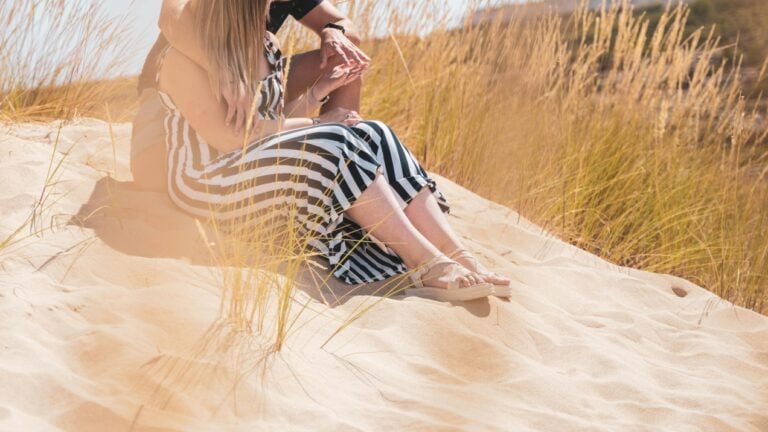 Un couple est assis dans les dunes, les mains entrelacées, prêt à vivre une histoire érotique brûlante.