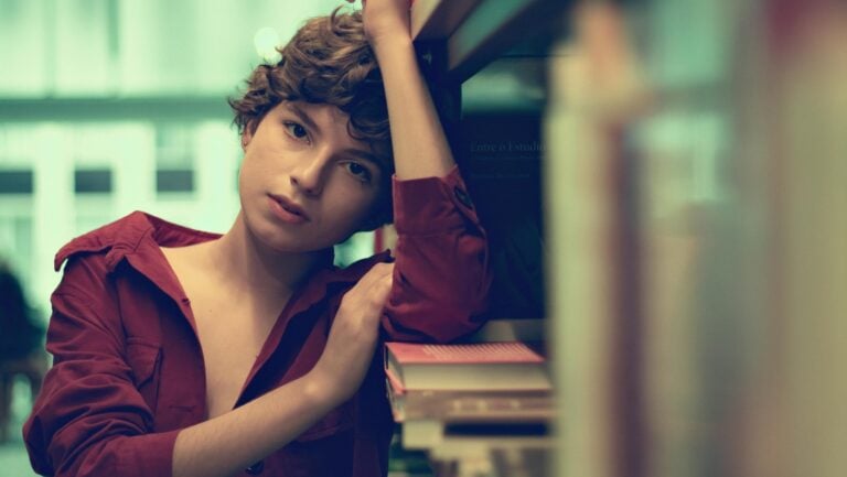 Une jeune femme est accoudée contre dans livres dans une bibliothèque. Sa chemise est ouverte, elle ne porte pas de soutien gorge, prête à vivre une histoire érotique.