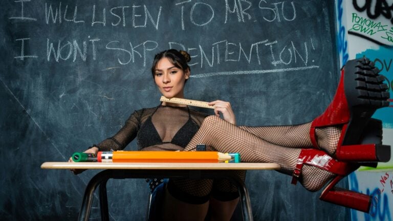 Une professeur très sexy est assise les jambes croisées sur son bureau, en attente d'un parent pour vivre une histoire érotique.