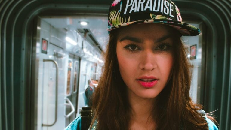 Une jeune femme avec de long cheveux bruns et une casquette est dans le train, prête a vivre une histoire érotique digne de ce nom.