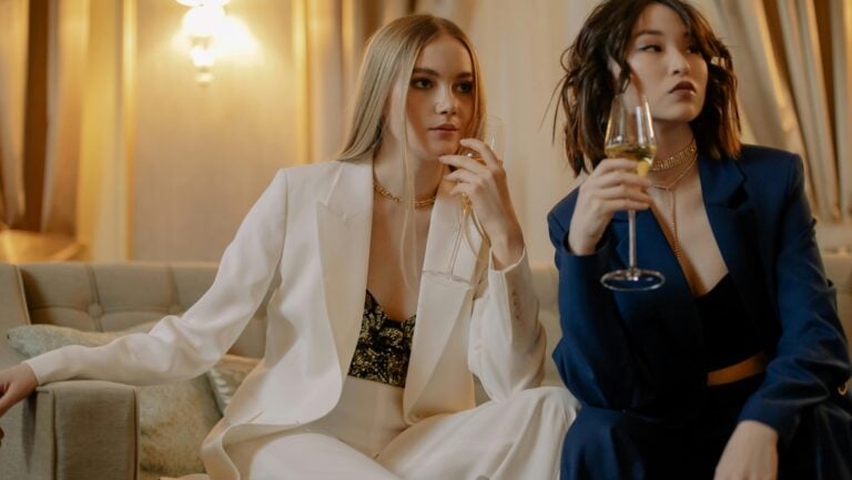 Deux femmes sont assises sur un canapé dans une chambre d'hôtel, un verre de vin à la main, prêtes à vivre une histoire érotique à trois.