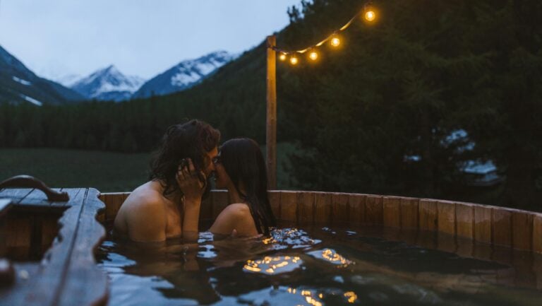 Un couple s'embrasse tendrement dans un jacuzzi extérieur, face aux montagnes, prêts à vivre une histoire érotique dans l'eau.
