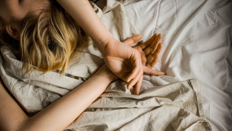 Une femme est allongée sur son lit, les bras au dessus de sa tête. Elle vit un orgasme féminin.