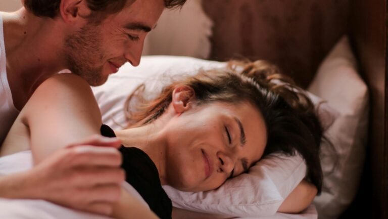 Deux personnes sont allongées souriant dans leur lit, en position de la cuillère.