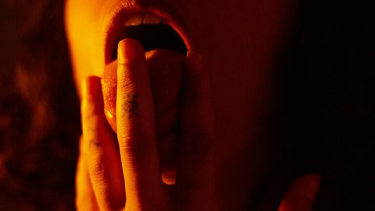 Une femme se lèche les doigts sensuellement dans la pénombre.