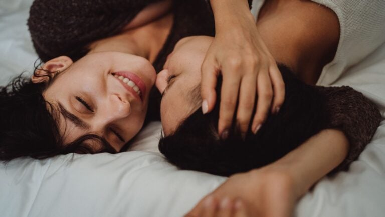 Un couple souriant est allongé dans leur lit, dans la position de l'éléphant.
