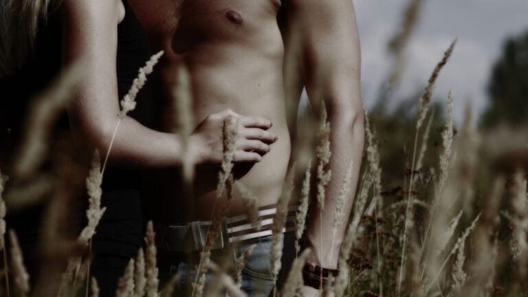 Un homme torse nu se fait caresser par une femme nue dans un champs.
