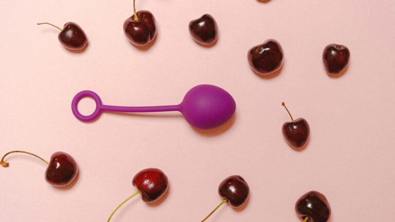 Un oeuf vibrant est photographié au milieu de cerises sur fond rose.