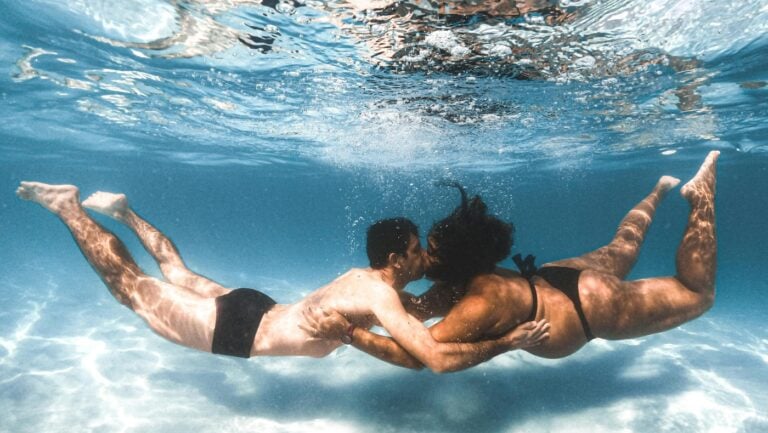 Un couple s'embrasse au fond de l'eau, se tenant les mains, une initiation romantique à faire l'amour dans l'eau.