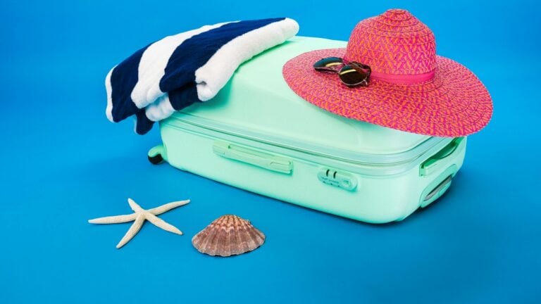 Un chapeau et une serviette rayée sont posés, sur une valise de couleur vive, afin d'illustrer les meilleurs sextoys à emporter avec soi en vacances.